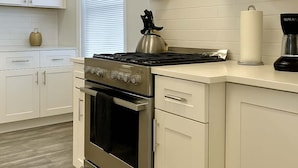 Una cocina moderna con armarios blancos, estufa de acero inoxidable y cafetera.