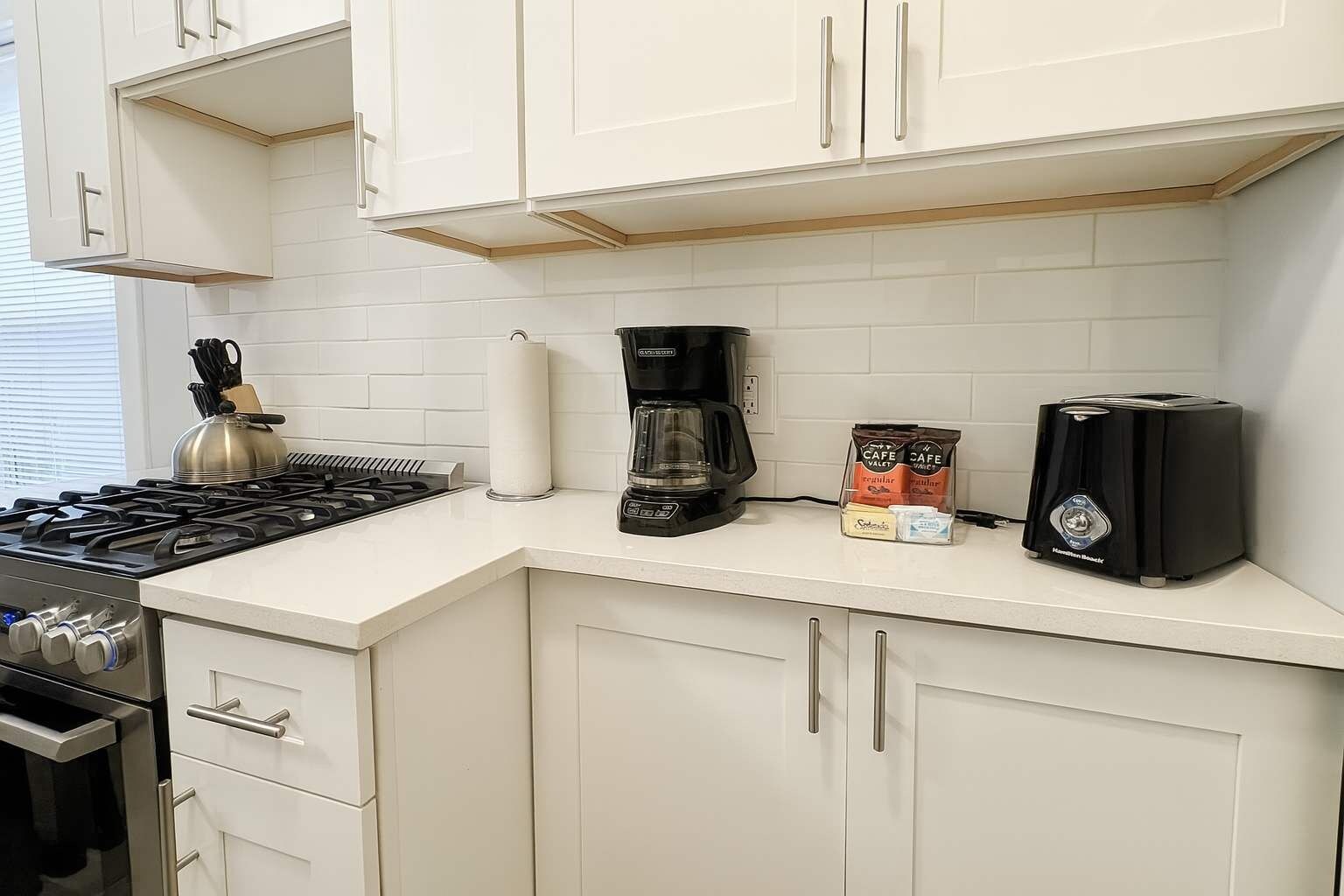 A kitchen with white cabinets, a gas stove, a coffee maker, and a toaster.