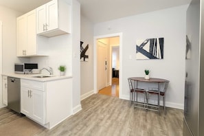A modern kitchen with white cabinetry, a dishwasher, and a microwave. There is a dining area with a table and chairs, and a staircase leading to another level.
