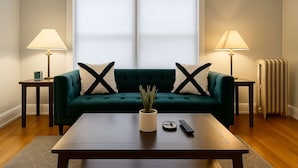 Una sala de estar con un sofá verde, dos lámparas, una mesita de centro y un radiador.