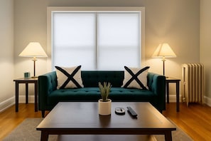 Ein Wohnzimmer mit einem grünen Sofa, zwei Lampen, einem Couchtisch und einer Heizung.