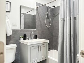 A modern bathroom with a white sink, mirror, and toilet. There is a shower with a curtain and a bathtub.