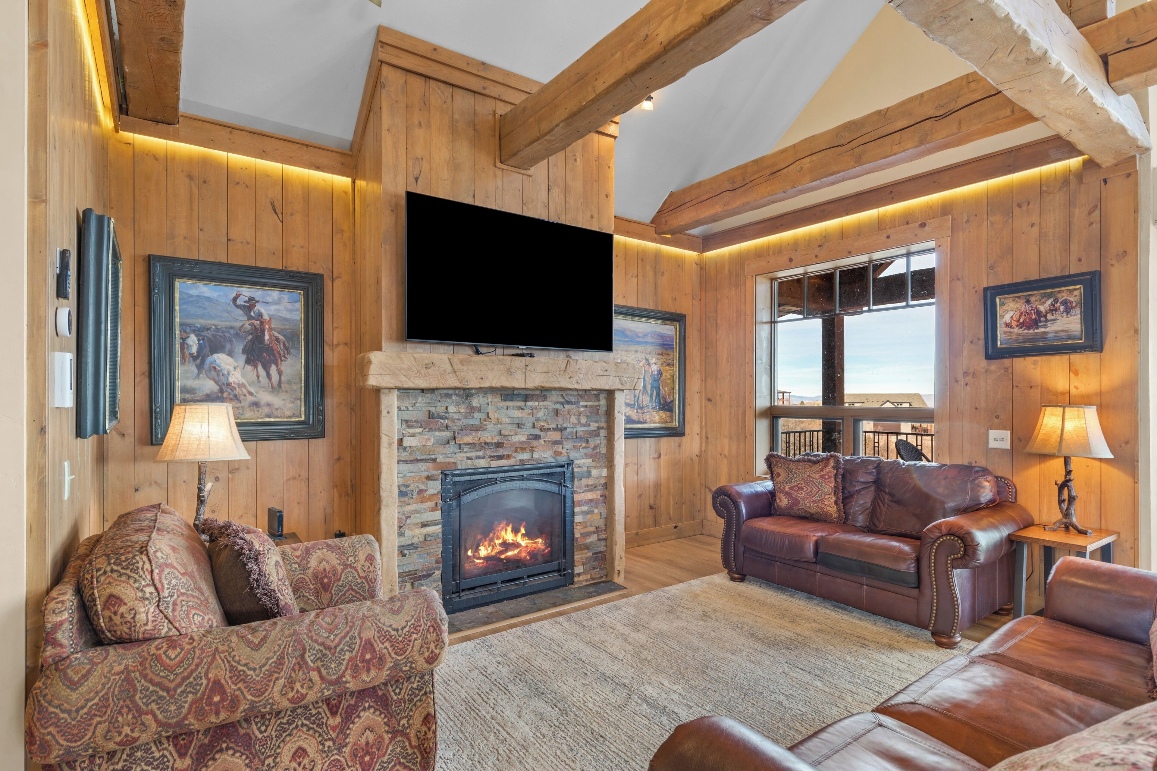 A cozy living room with a fireplace, leather sofas, wooden walls, and a large TV.