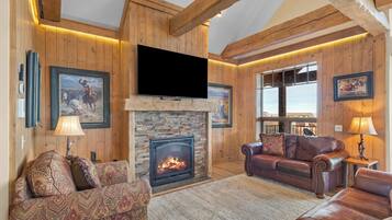 A cozy living room with a fireplace, leather sofas, wooden walls, and a large TV.