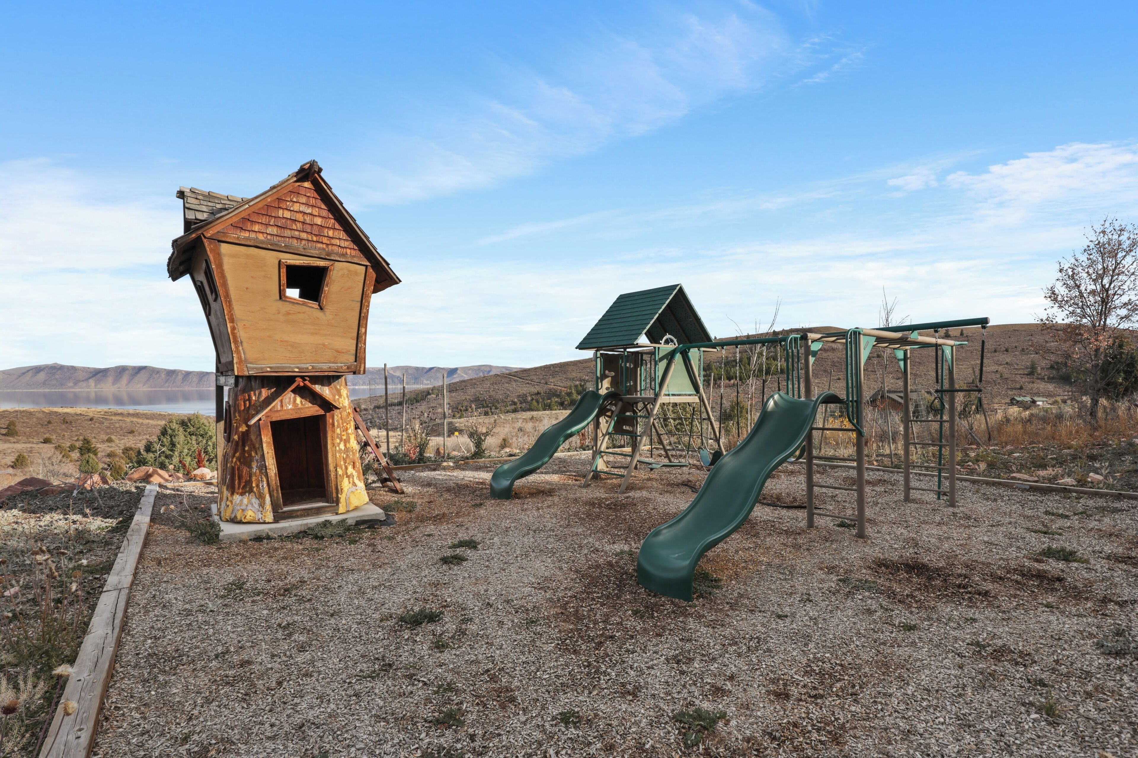 Un parque infantil con una casita de madera y toboganes, frente a un paisaje montañoso.