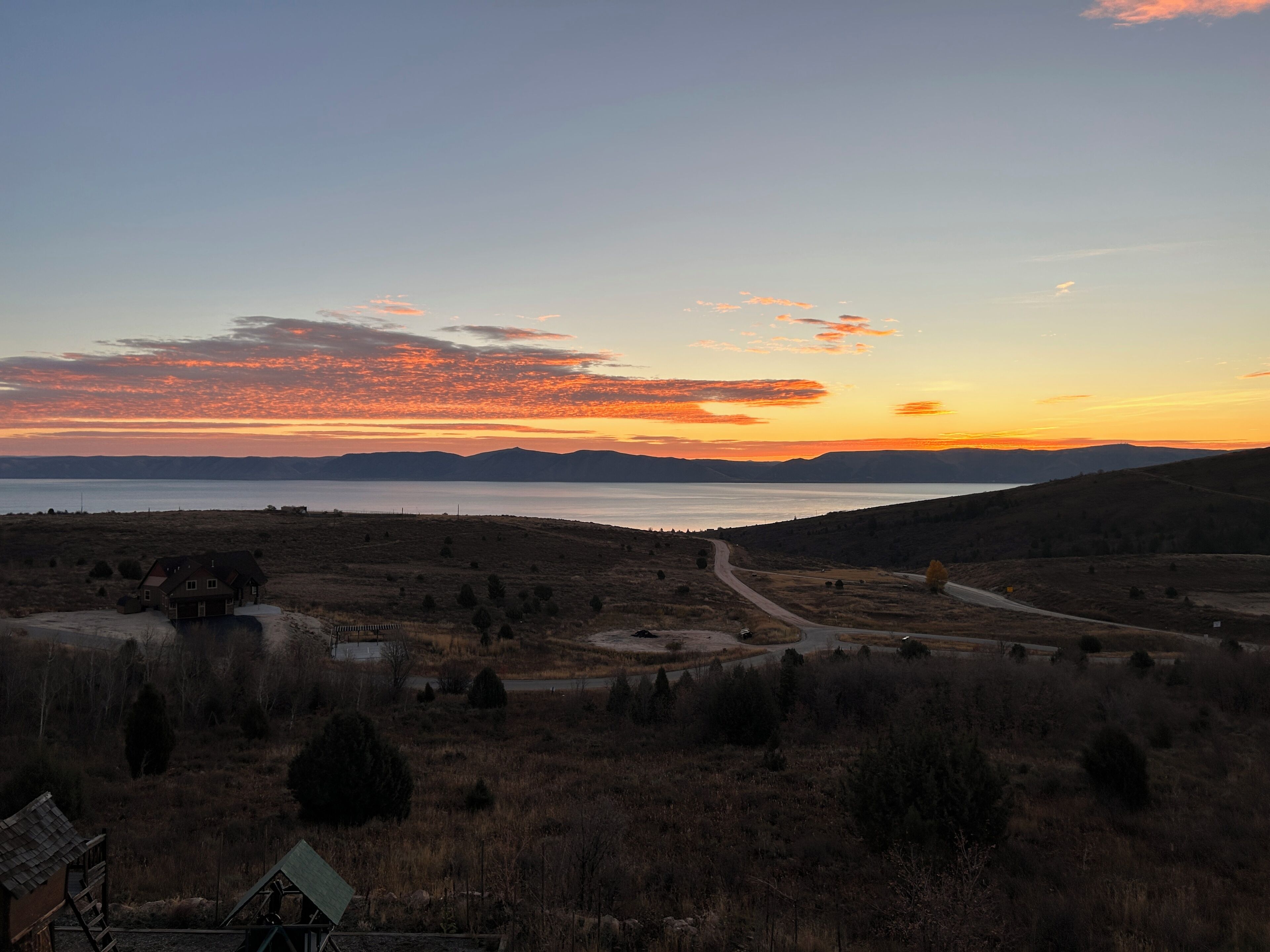 A landscape with a road, a body of water, and distant mountains during sunset.
