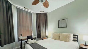 A hotel room with a large bed, a desk, a chair, and a ceiling fan. - Paradise 1BR Apt in Lincoln Park (Chicago)