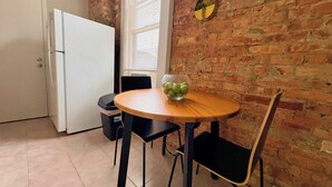 A small kitchen with a white refrigerator, a wooden table with a glass bowl of fruit, black chairs, and a brick wall. - Paradise 1BR Apt in Lincoln Park (Chicago)