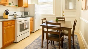 A compact kitchen with wooden cabinets, a stove, microwave, and a dining table with chairs. - Cozy 3BR Gem in North Center (Chicago)
