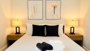 A neatly made bed with white and black linens, two bedside lamps, and two abstract art pieces on the wall. - Cozy 3BR Gem in North Center (Chicago)