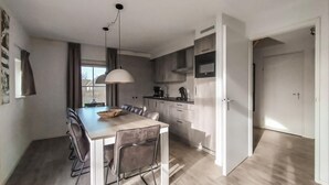 A modern kitchen with a dining area, featuring a large table, chairs, and a hanging light fixture. - Beautiful home in Den Ham with sauna (Den Ham)