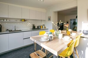 A modern kitchen with white cabinets, a wooden dining table, and yellow chairs.