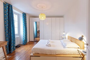 A bedroom with a wooden bed, white bedding, a bedside lamp, and a hanging light fixture.