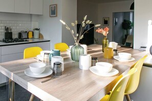 A modern kitchen with white cabinets, a wooden countertop, and yellow chairs. There are various kitchen appliances and utensils on the counter.