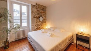 Ein Schlafzimmer mit Steinwand, großem Fenster, Nachttisch mit Lampe und Bett mit gerollten Handtüchern.