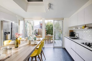 A modern kitchen with a dining area, large windows, and a view of the outdoors.