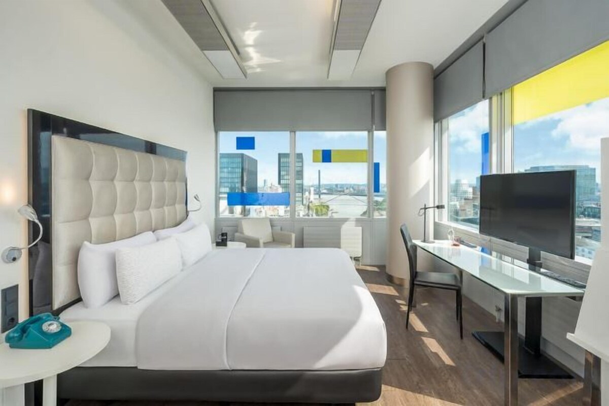 A modern hotel room with a large bed, a desk, and a TV.