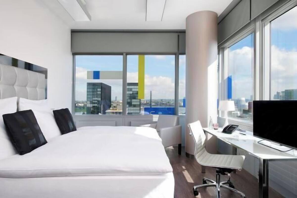 Ein modernes Hotelzimmer mit einem großen Bett, einem Schreibtisch und Blick auf die Stadtlandschaft.