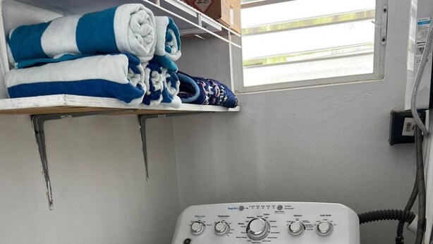 Une petite machine à laver blanche à chargement frontal, installée dans un petit espace buanderie avec une fenêtre au-dessus.
