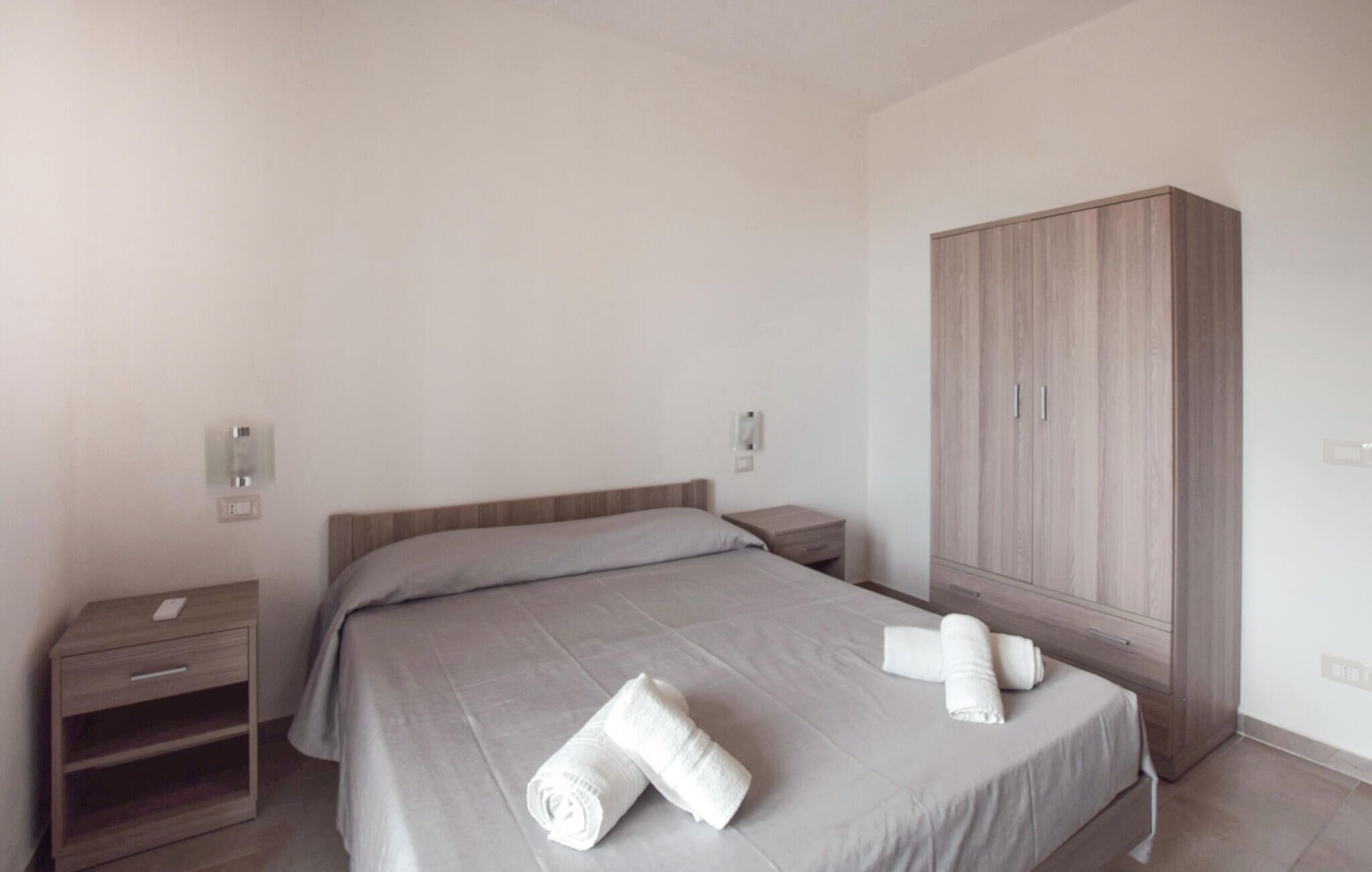 Una camera da letto con un letto, un comodino, un armadio e due interruttori a parete.
