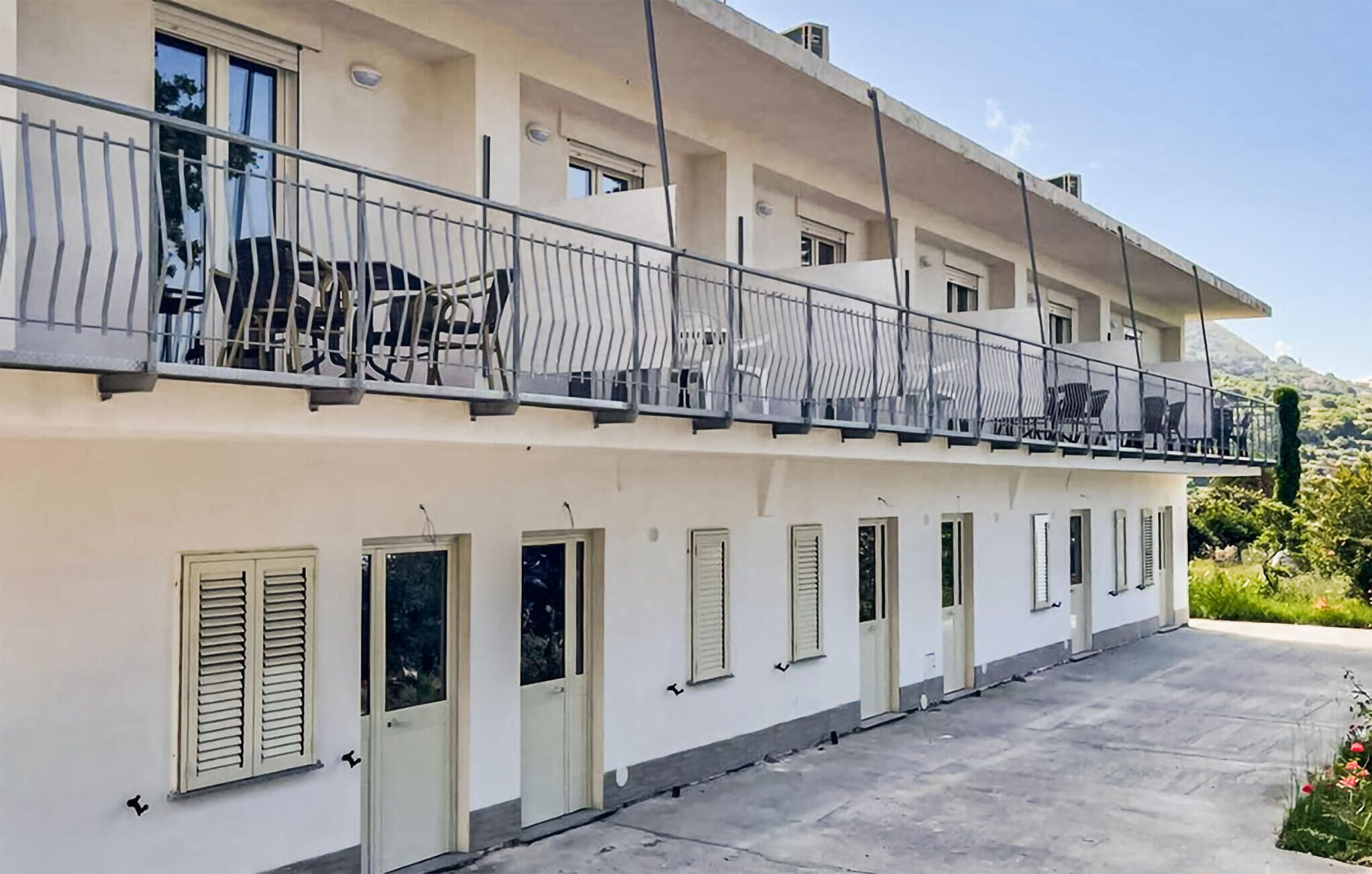 A multi-story building with balconies, windows with shutters, and a paved ground.