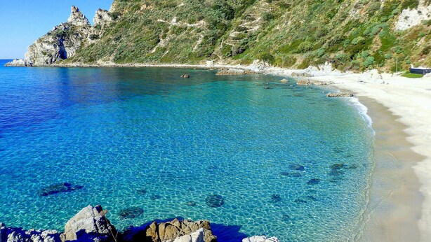A coastal beach with clear blue water, rocky shore, and a hillside with vegetation. - Cozy apartment in Ricadi with WiFi (Ricadi)