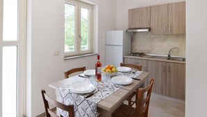 A compact kitchen with a dining area, featuring a window, a refrigerator, a stove, and wooden cabinets. - Cozy apartment in Ricadi with WiFi (Ricadi)