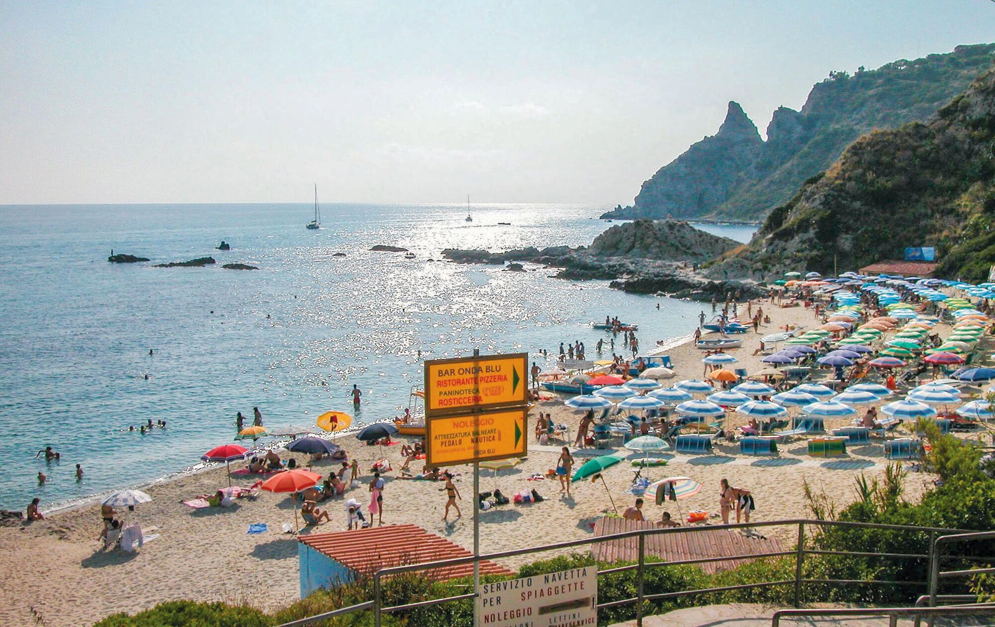 Uma praia movimentada com muitos guarda-sóis e pessoas aproveitando o sol.