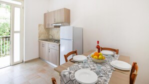 A compact kitchen with a refrigerator, sink, and wooden cabinets. A dining table with chairs and a fruit bowl is set for a meal. - Gorgeous apartment in Ricadi (Ricadi)