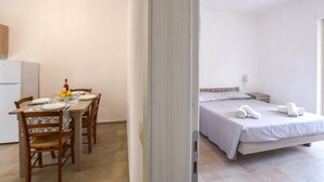 A compact room with a bed, a small bedside table, and a dining area with a table set for two. - Gorgeous apartment in Ricadi (Ricadi)