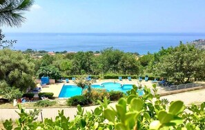 A pool area with a view of the sea, surrounded by greenery and blue lounge chairs. - Gorgeous apartment in Ricadi (Ricadi)