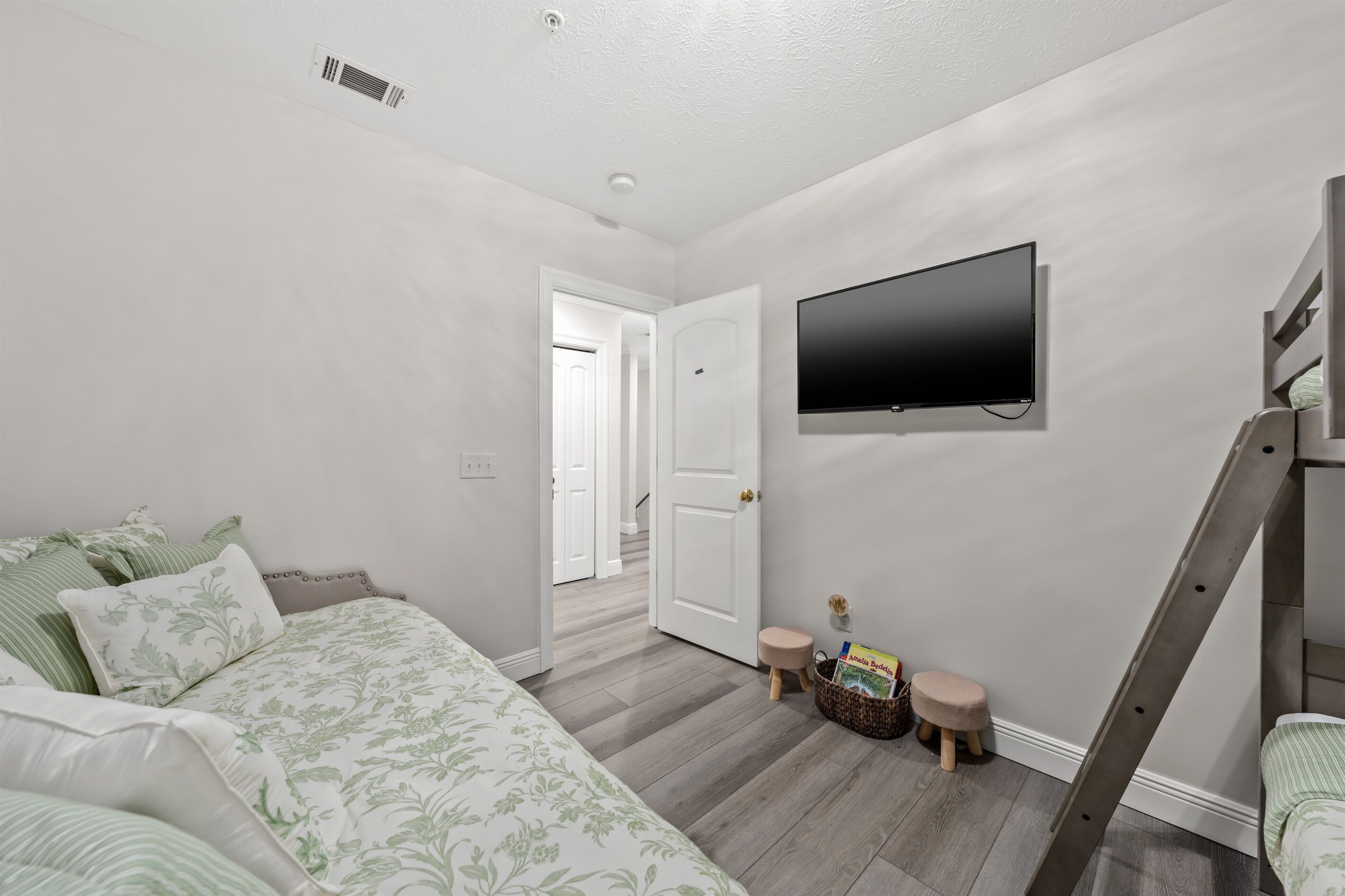 Un dormitorio con una cama, un televisor montado en la pared, una escalera de madera y una puerta que da a otra habitación.