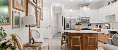 A modern kitchen with white cabinetry, a central island with stools, and a dining area with a chair and table.