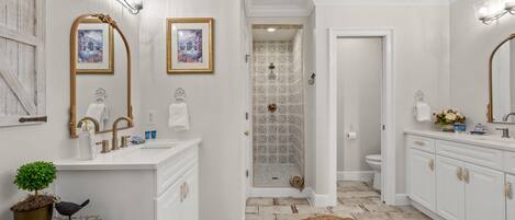 Un baño con muebles blancos, un espejo grande y una ducha con azulejos estampados.