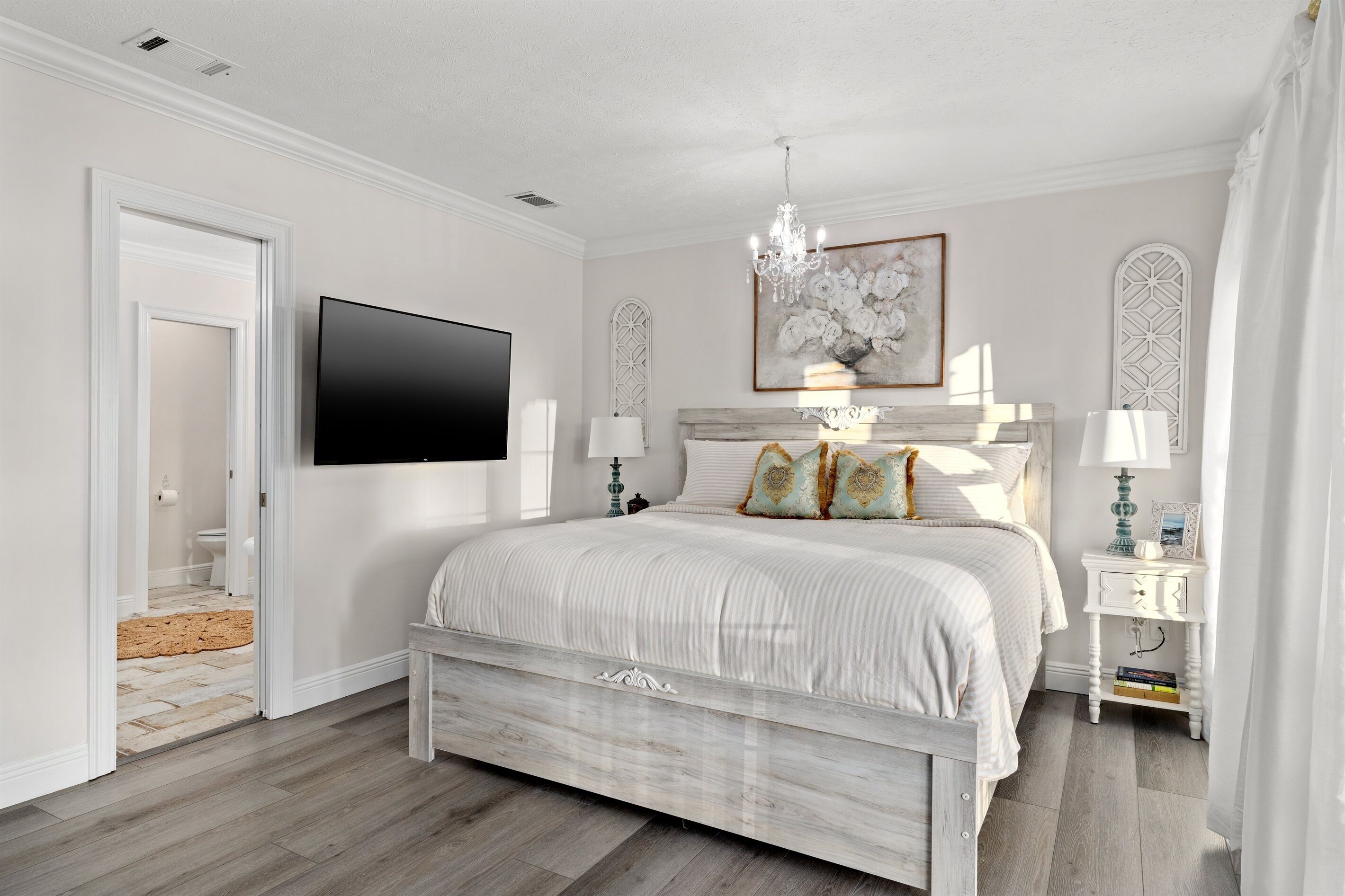 Un dormitorio con una cama, televisión, candelabro y un cuadro en la pared.