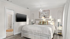 Une chambre à coucher avec un lit, une télévision, un lustre et un tableau au mur.