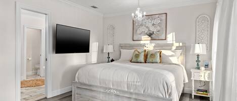 Un dormitorio con una cama, televisión, candelabro y un cuadro en la pared.