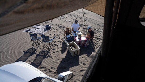 A sandy beach with a table and chairs, a cooler, and a white vehicle. - The Shepherd Company (Coyhaique)