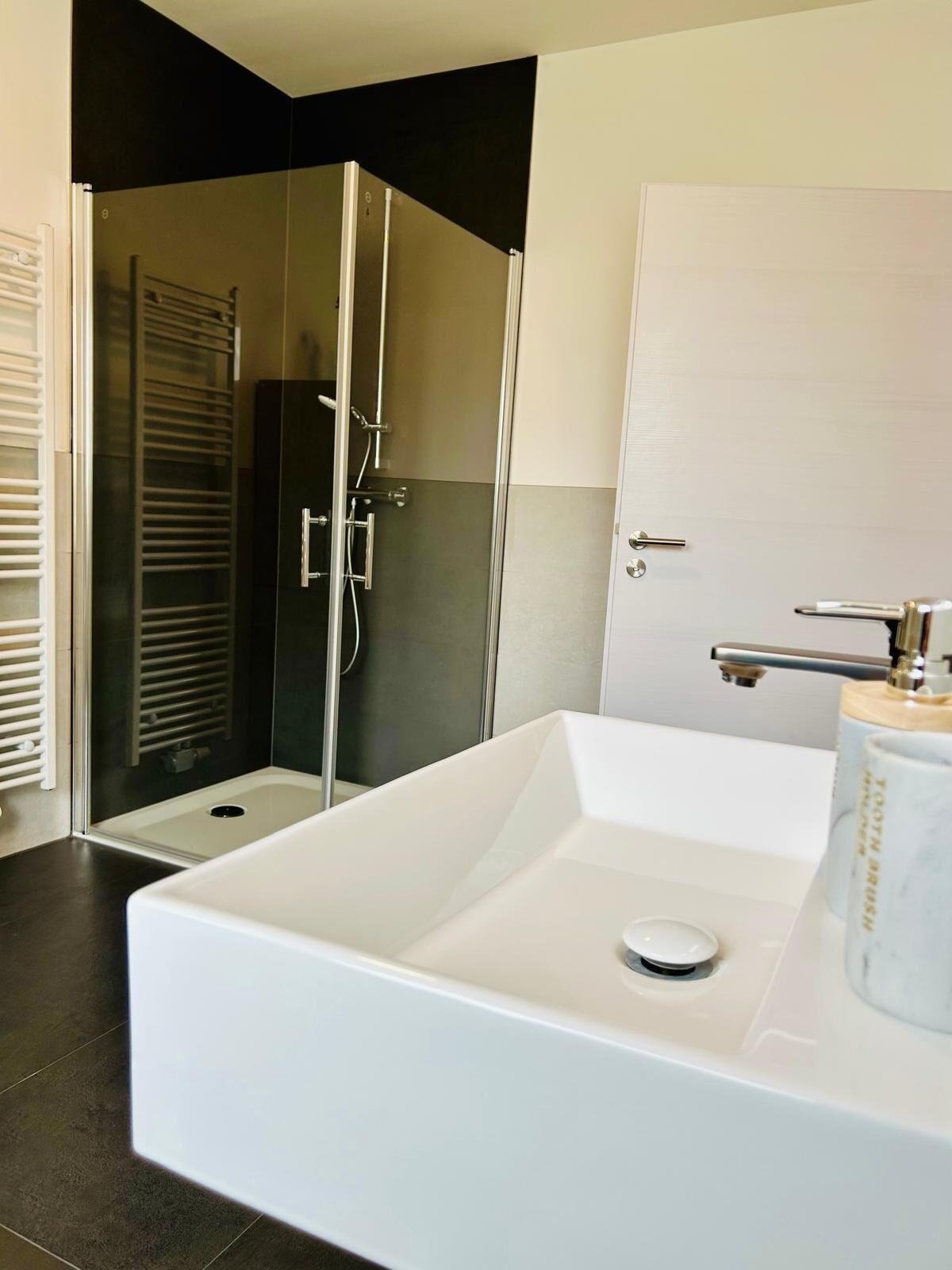 A modern bathroom with a large white bathtub, a glass shower enclosure, and a white door.