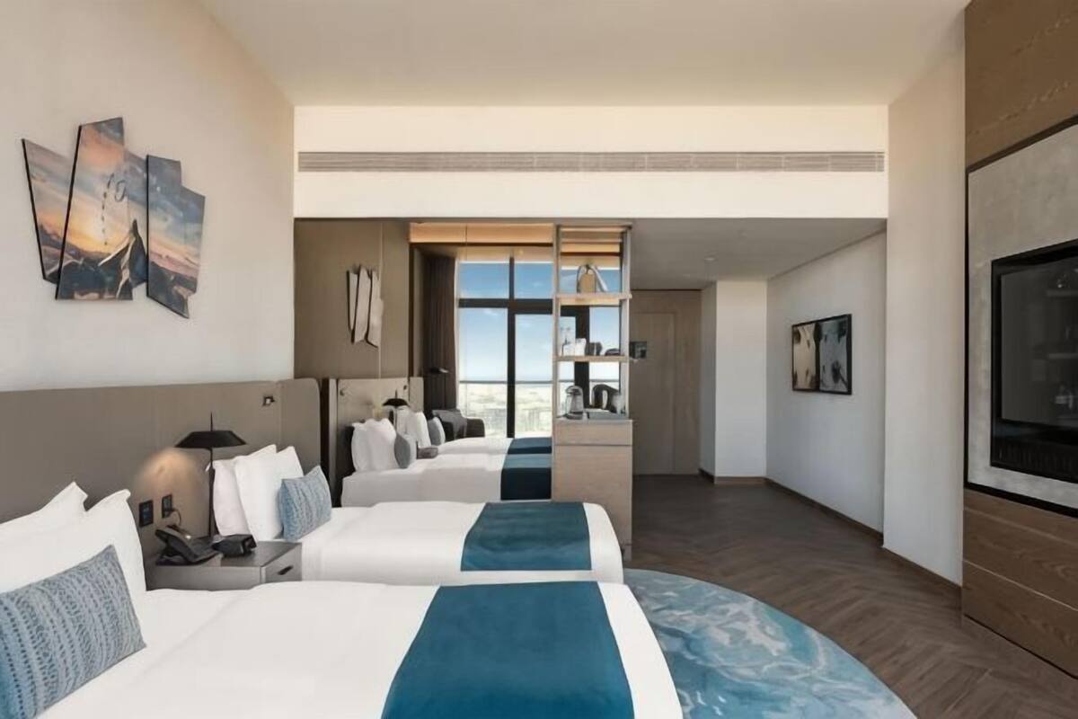 A hotel room with two beds, a TV, artwork, and a view of the city.