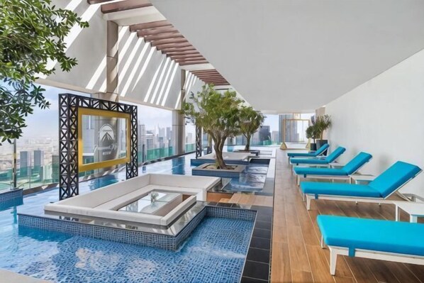 A rooftop infinity pool with blue-tiled flooring, sun loungers, and a view of the city skyline. - Paramount Hotel Midtown (Dubai)