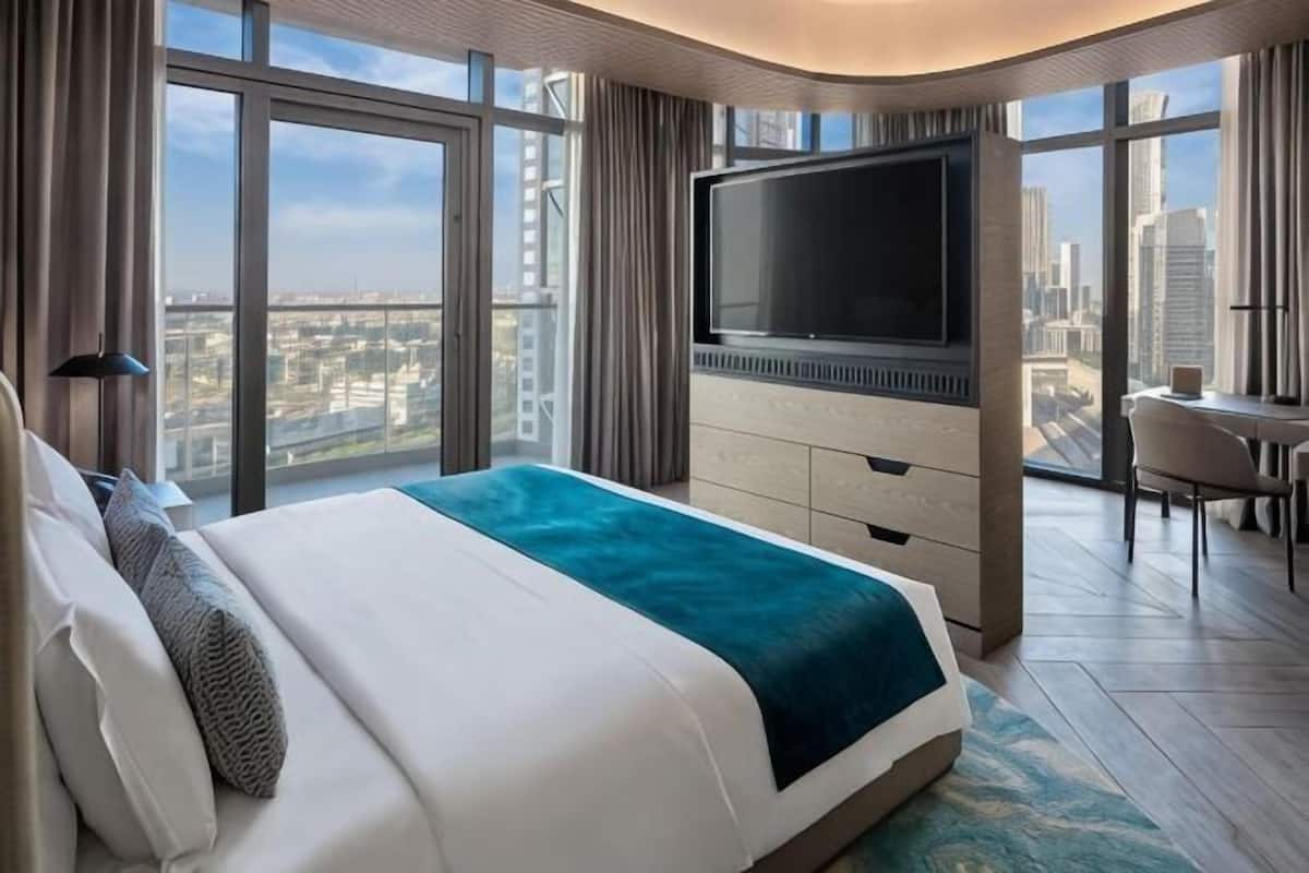 Une chambre dâhĂŽtel moderne dotĂ©e dâun grand lit, dâune tĂ©lĂ©vision Ă Ă©cran plat, dâun bureau et offrant une vue sur la ville.