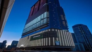 A modern skyscraper with a prominent digital display on the facade, surrounded by other high-rise buildings. - Paramount Hotel Midtown (Dubai)