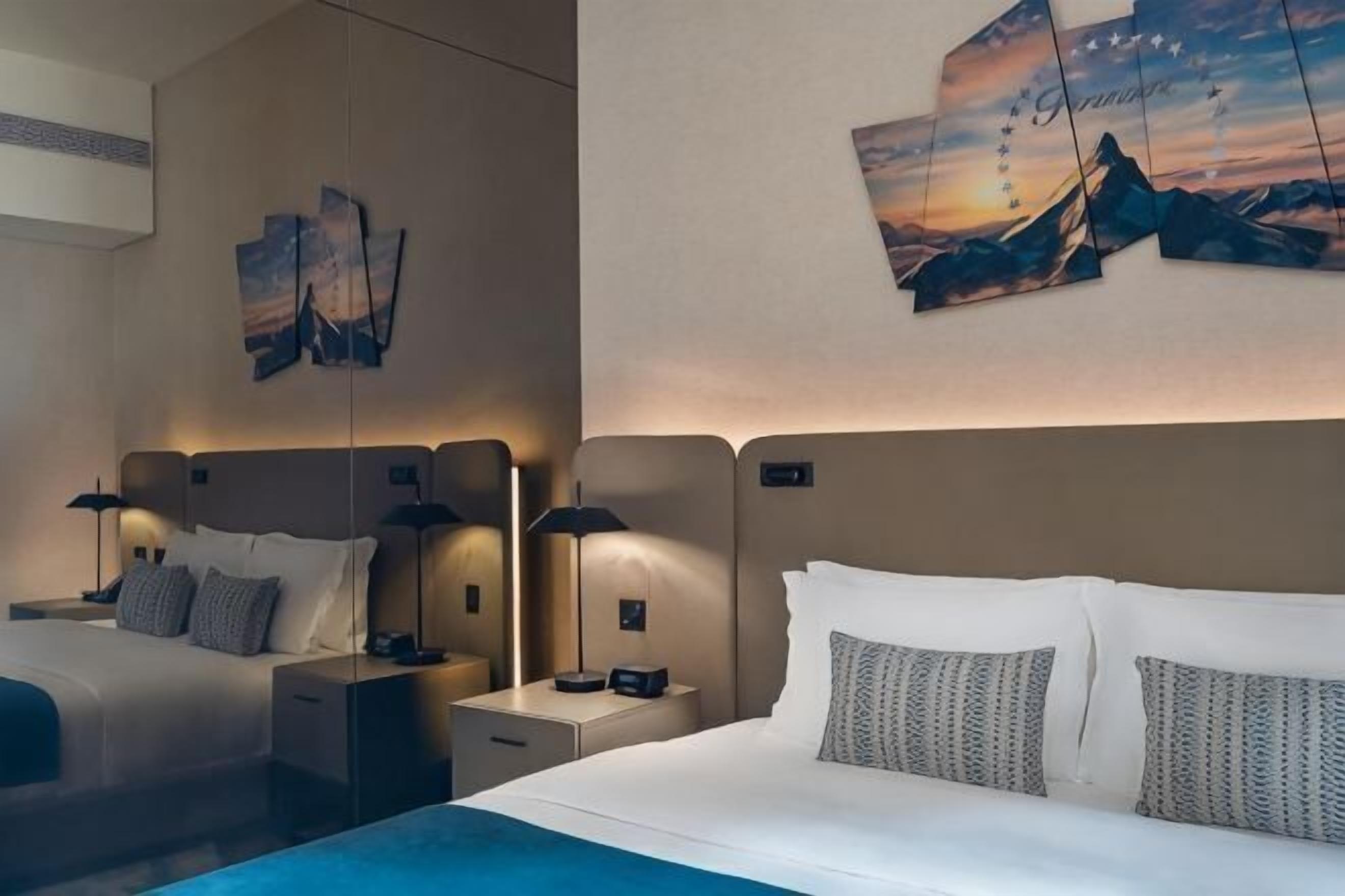 A hotel room with two beds, nightstands, lamps, and artwork on the walls.