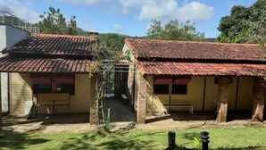 Twee gelijkvloerse gebouwen met rode pannendaken, een gazon en een kleine tuin.