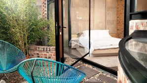 Een slaapkamer met een bed en een glazen deur die uitkomt op een buitenruimte met stoelen en planten.