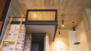 Een loft-achtige kamer met openliggende bakstenen muren, een houten ladder en een zwevend houten platform.