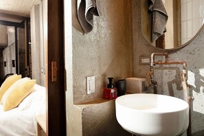 A bathroom with a white sink, a mirror, a towel hanging on the wall, and a bed with yellow pillows. - CASA MACARENA (Bogotá)