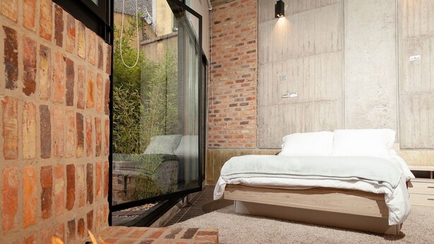Een slaapkamer met een metselwerk open haard, een groot raam en een bed met witte beddengoed.