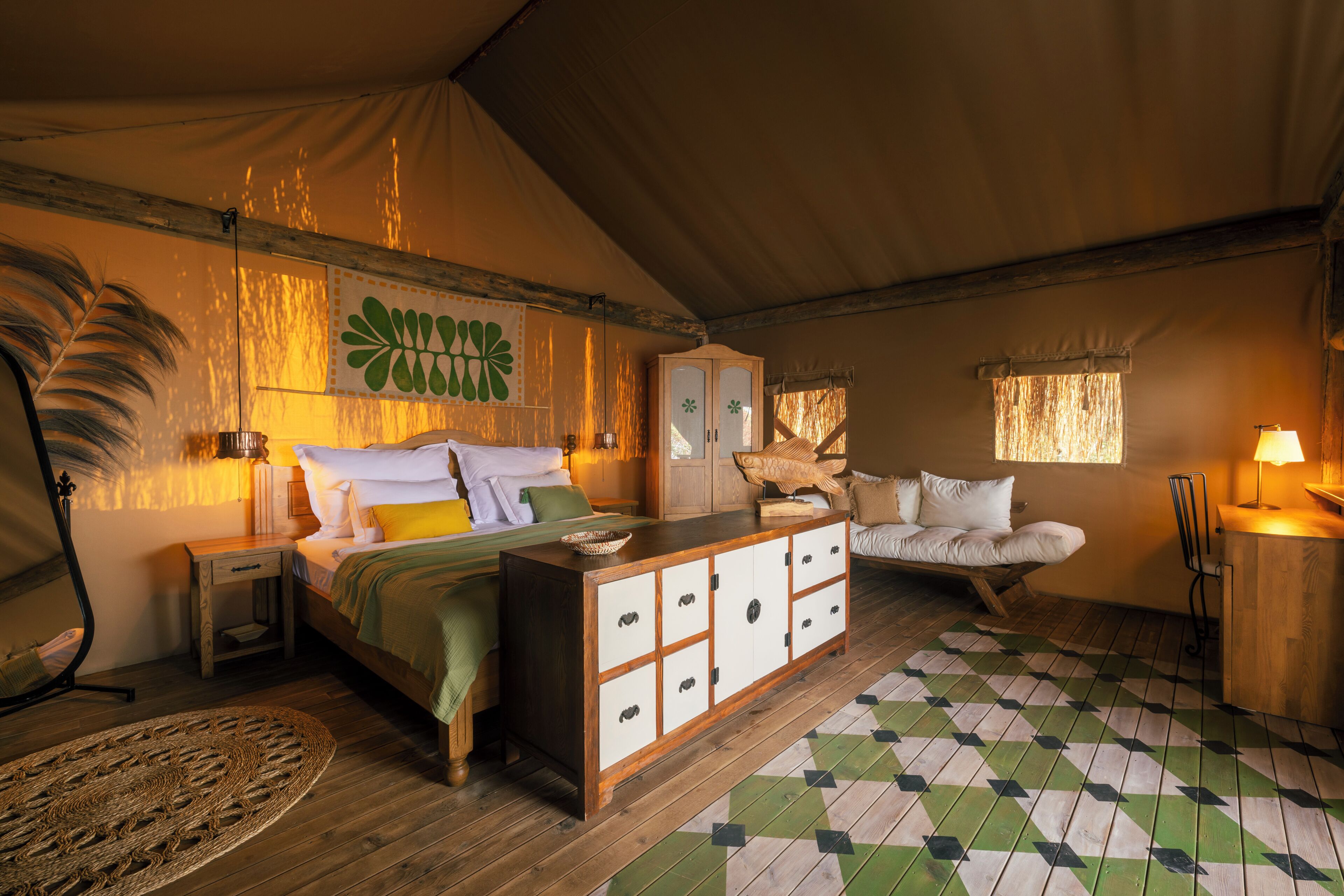 A tented accommodation with a bed, a wooden cabinet, a sofa, and a dining area.